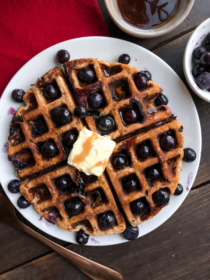 Paleo blueberry waffle with blueberries and butter on top on a white plate