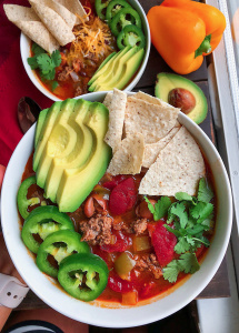 taco soup in a white bowl with avocado, chips, cilantro,