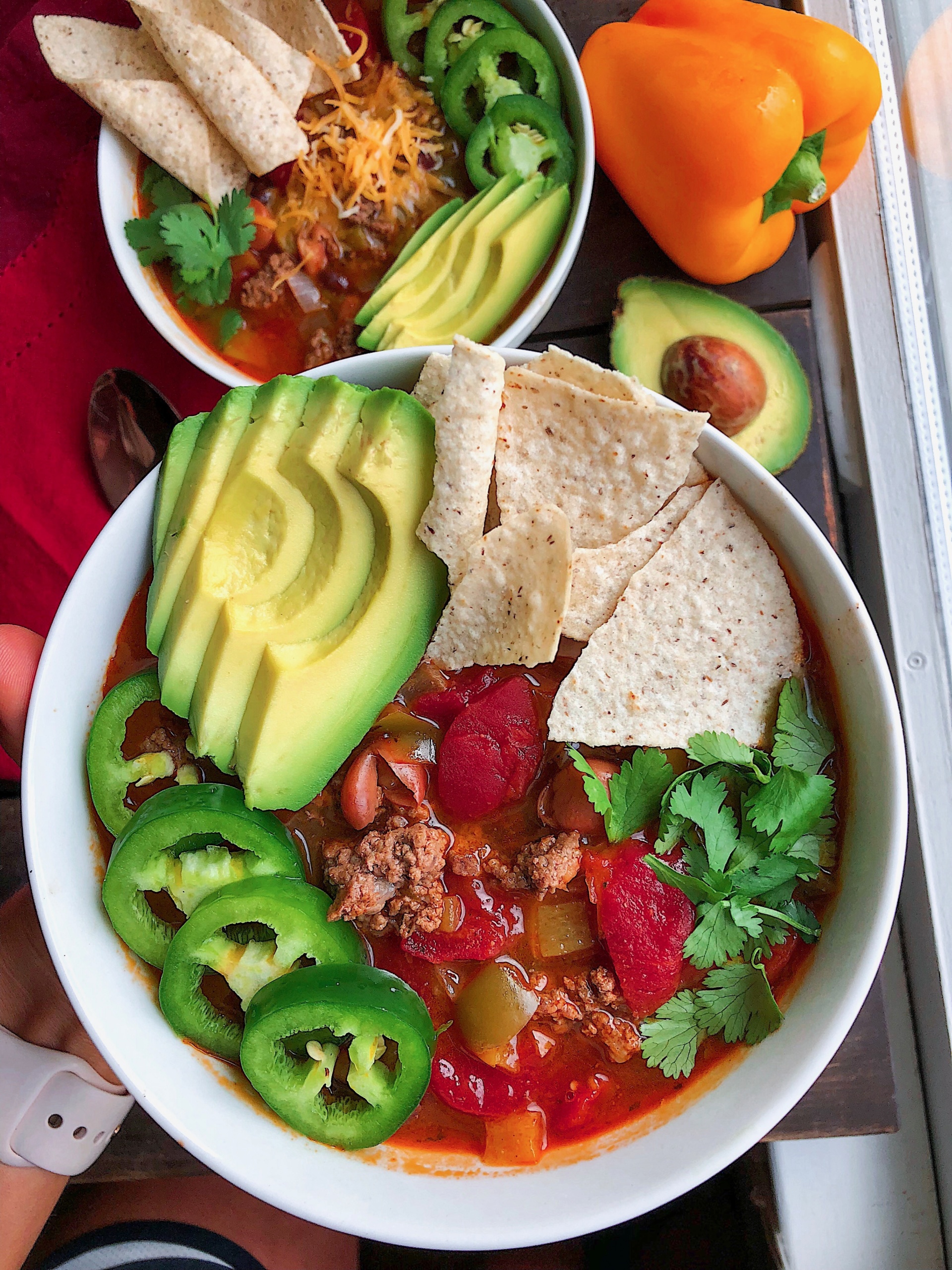 taco soup in a white bowl with avocado, chips, cilantro,