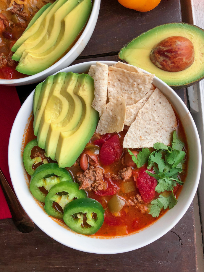 taco soup in a white bowl with avocado, chips, cilantro,