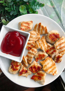 healthy grilled chicken nuggets on a white plate with ketchup