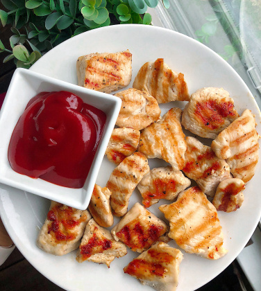 healthy grilled chicken nuggets on a white plate with ketchup