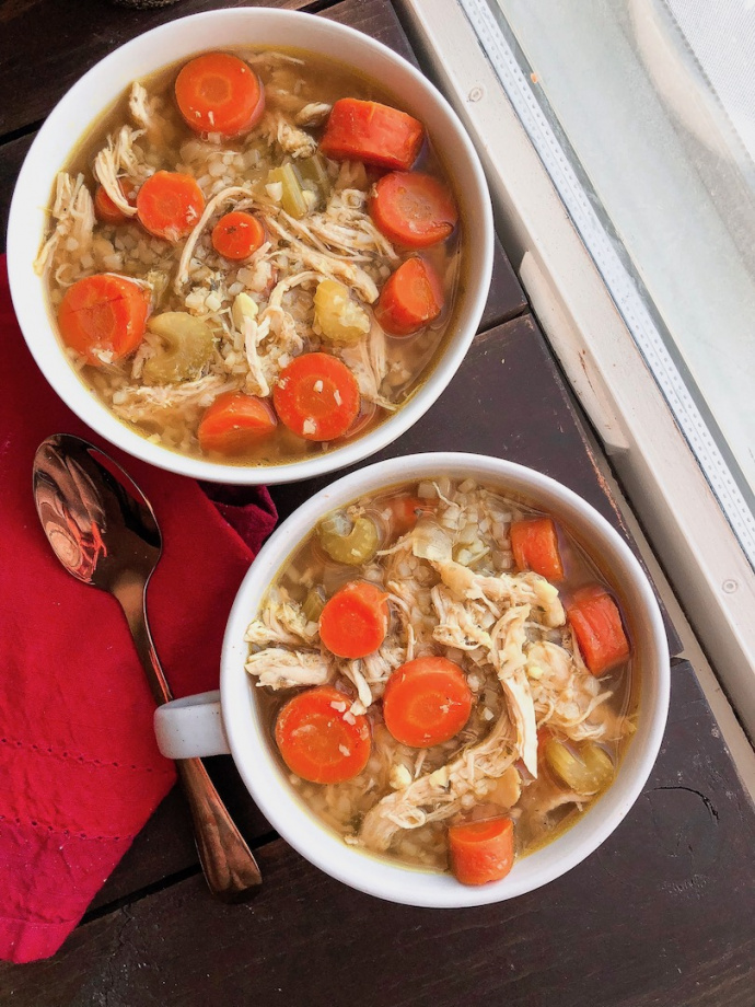 healthy chicken and rice soup with cauliflower rice and carrots in a white bowl 