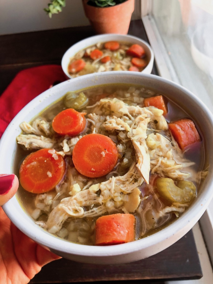 healthy chicken and rice soup with cauliflower rice and carrots in a white bowl