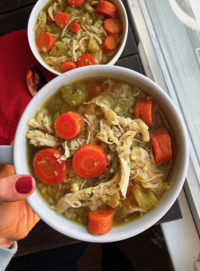 healthy chicken and rice soup with cauliflower rice and carrots in a white bowl